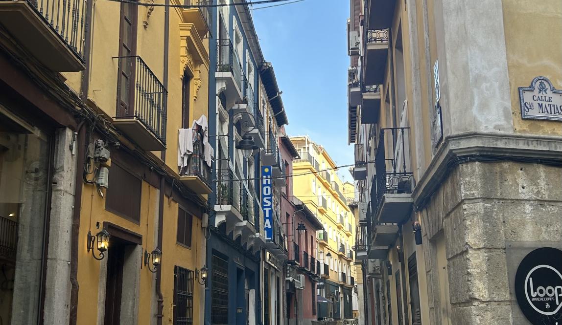 A narrow story street with two yellow buildings on either side.