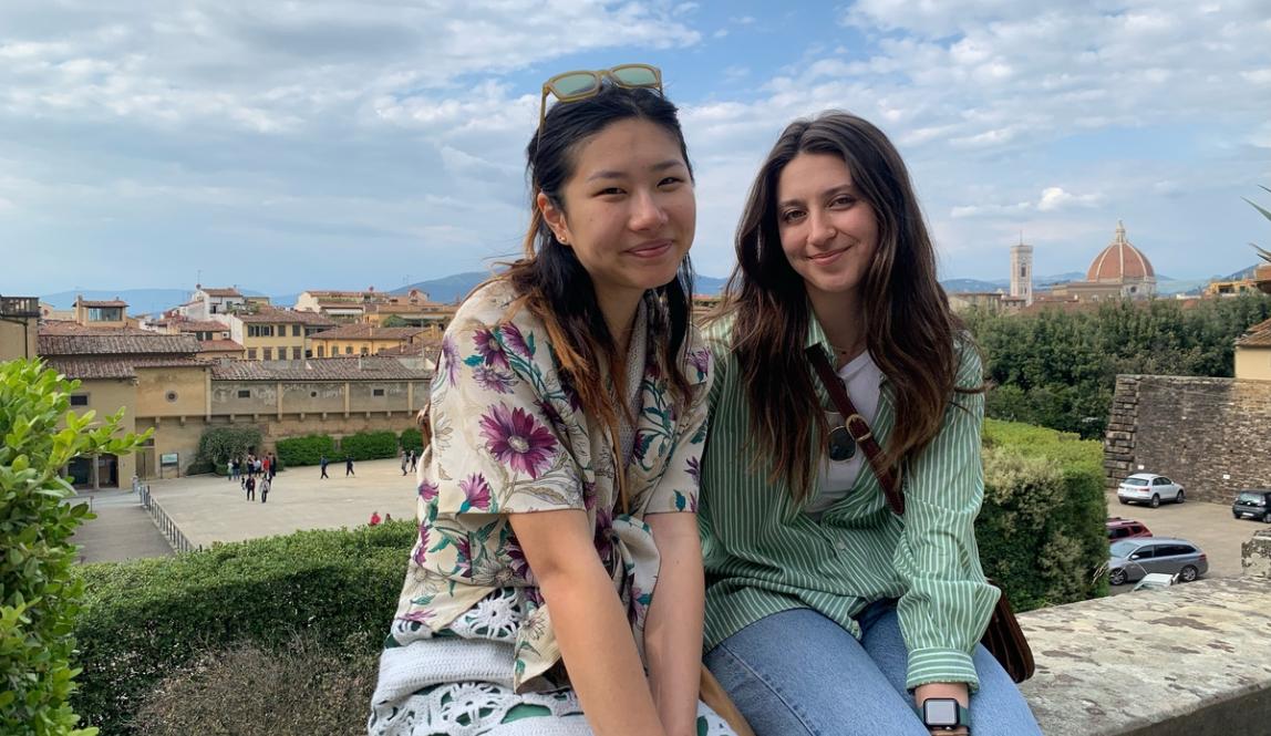 Two girls sitting on a ledge in Florence italy with the city behind them and clouds