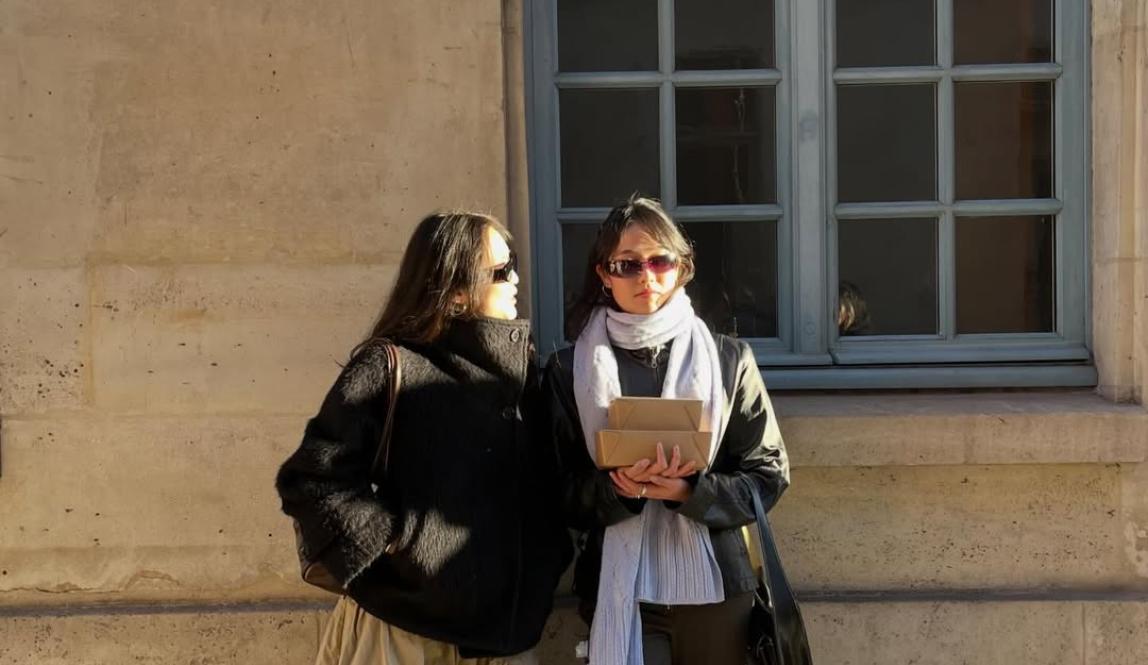 Two students holding books against a wall 