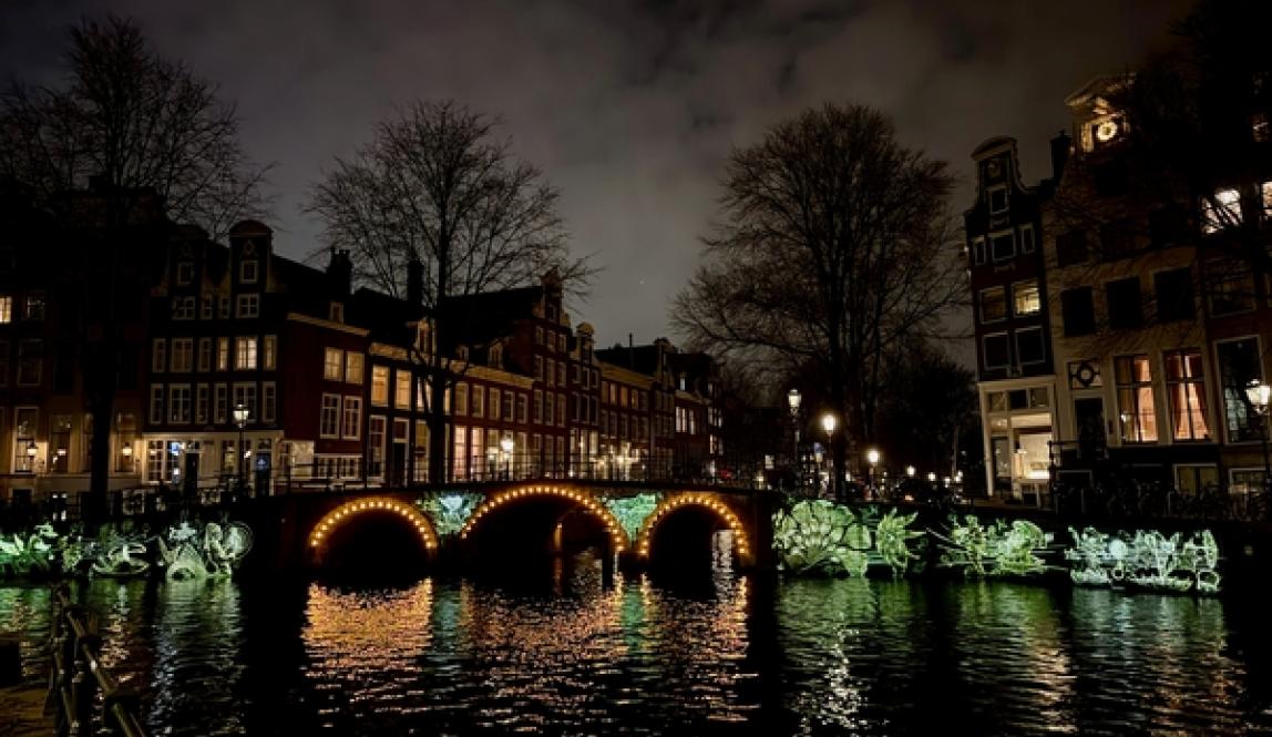 Amsterdam Canal at night with a glowing bridge, reflections on the water, and historic buildings lining the waterfront