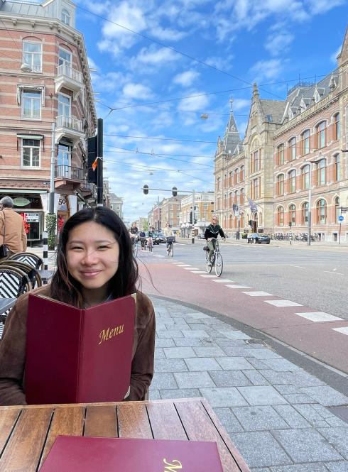 a student sitting on an outdoor restaurant patio with a menu in Amsterdam