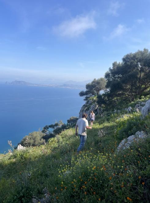 Two students hiking on a grassy mountain near the Mediterranean coast in Italy.