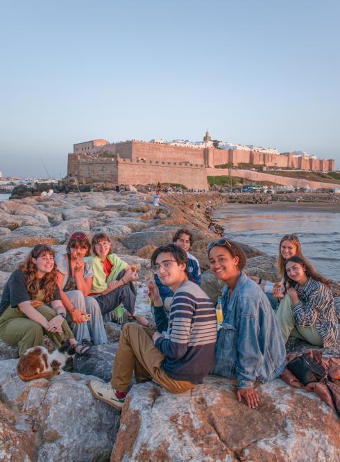 a group of students sitting near the beach with Rabat city in the background