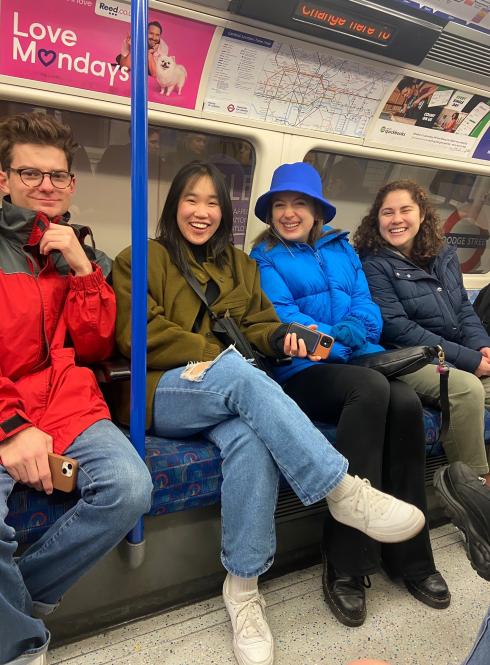 four students sitting on seats in the london tube passing a station