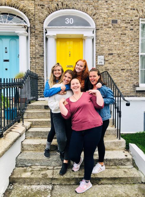 students standing on steps in front of a large door hugging and smiling