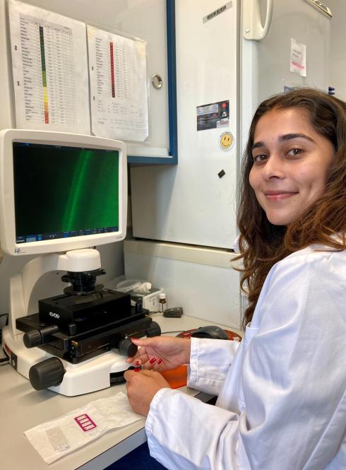 student in white coat sitting at desk in front of microscope and computer
