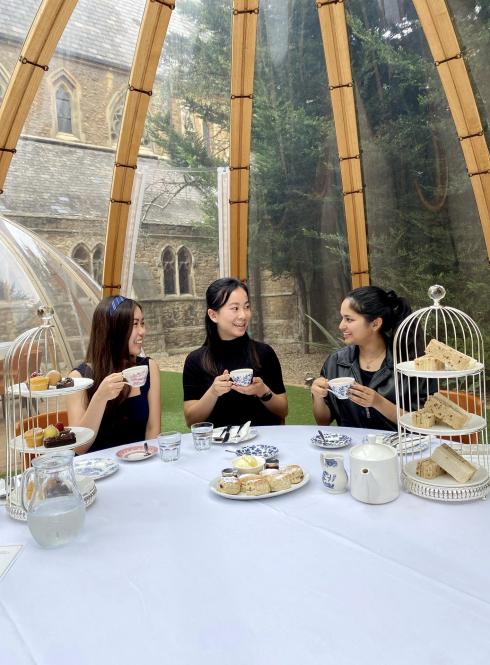 students sitting at white tableclothed setting with tea and assorted breads on elevated plates