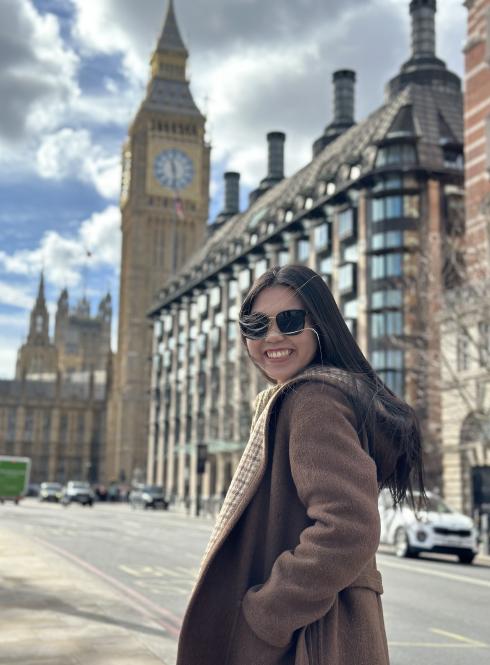 student in jacket and sunglasses walking down a sunny sidewalk towards big ben
