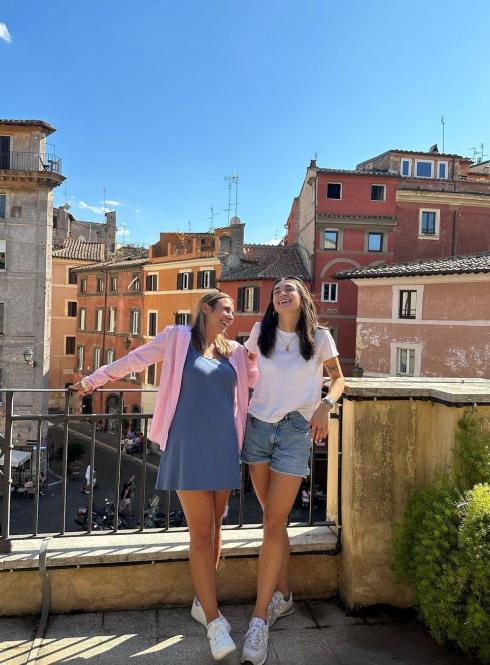 Two students stand next to eachother laughing on a sunny rooftop in Rome.