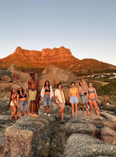 students standing on rocks in front of large flat-topped mountain at sunset