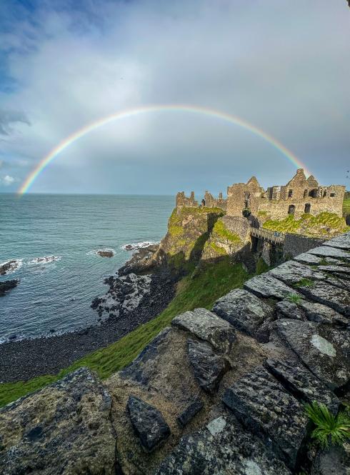 rocky cliffs with large body of water in background and giant rainbow in sky