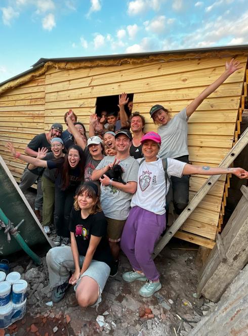 a group of students pose for a photo with a transitional home they built for a family in need