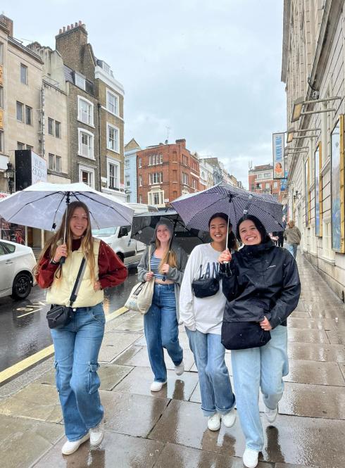 group of students walking on sidewalk with umbrellas