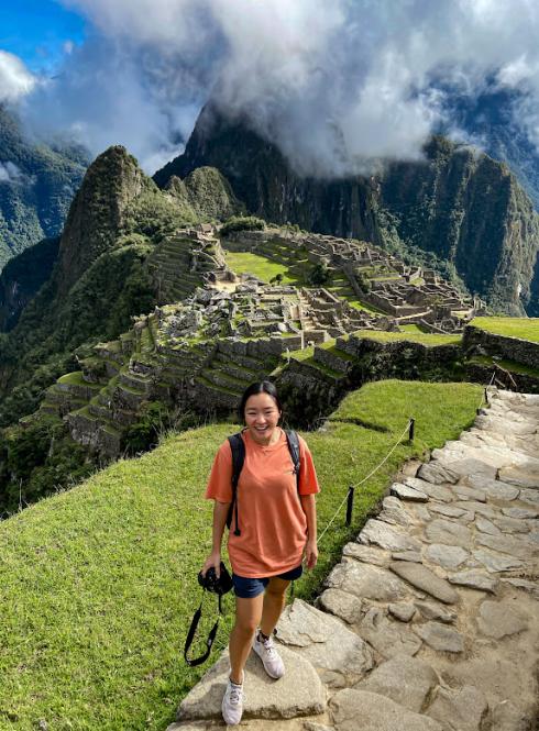 a student posing for a photo with great views of Machu Picchu and mountains in the background on a blue and cloudy day
