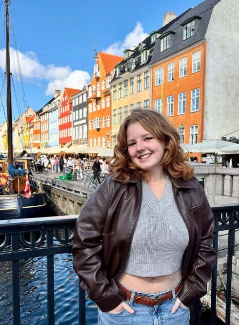Female student smiling with a backdrop of colorful buildings and a river in Amsterdam 