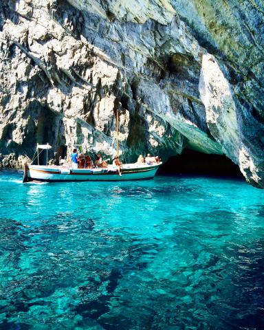 Rock arch and boat on Capri coast. Crystal-clear blue water and rugged cliffs. This alt text was added with Al; accuracy may vary.
