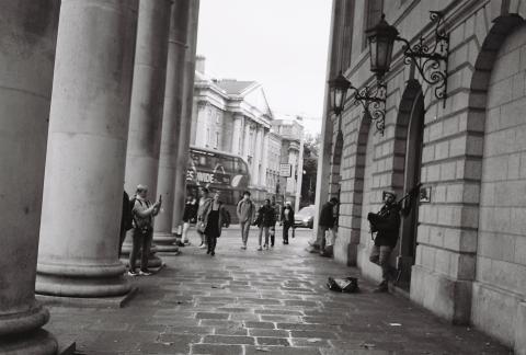 A tilted image portrays a lad playing bagpipes adjacent to an onlooking passerby