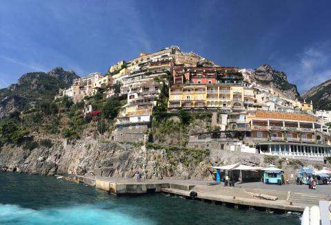 Colorful buildings on cliffs by the sea in Positano under a clear blue sky. This alt text was added with Al; accuracy may vary.