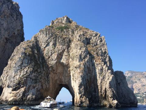 Stone arch formations rise from the sea under a clear blue sky near Capri. This alt text was added with Al; accuracy may vary.