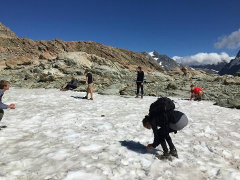 People having a snowball fight on a snowy mountain terrain under a clear blue sky. This alt text was added with Al; accuracy may vary.