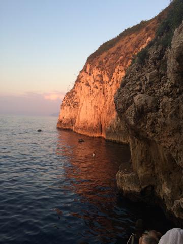 Rocky cliff at sunset with a calm sea below. This alt text was added with Al; accuracy may vary.