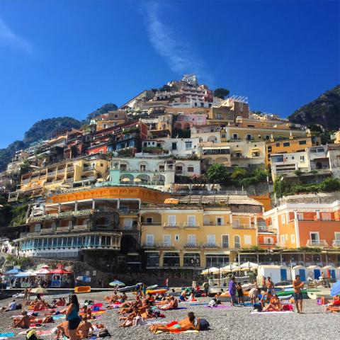 Colorful buildings on Positano's hillside overlooking a busy beach and blue sea. This alt text was added with Al; accuracy may vary.