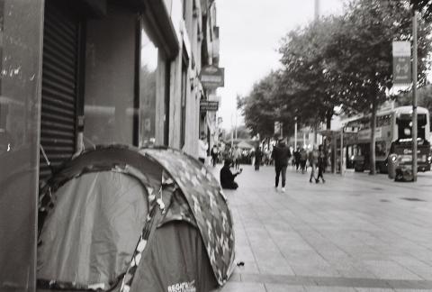 A tent, and in the background a person on their knees holding a cup out. 