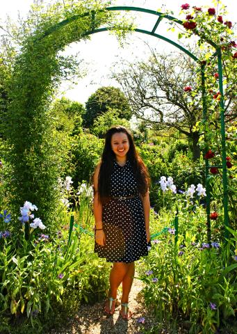 student in polka-dot dress smiles underneath an archway covered in vines