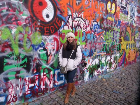 student standing in front of graffitied wall along cobblestone street