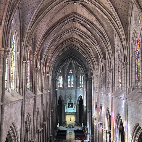 The interior of the Basílica del Voto Nacional. Arched ceiling with large stained glass windows.