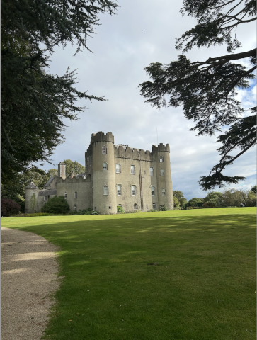 The back of Malahide Castle, a stone fortress with three stories and several towers, on a luscious green lawn.