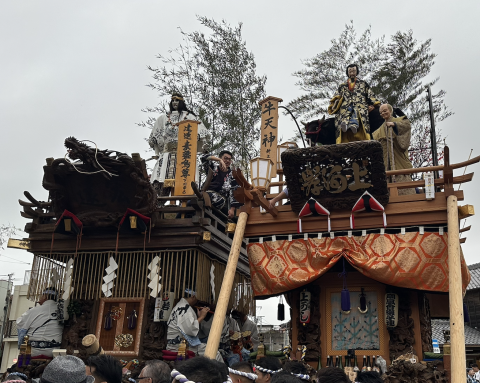 Two of the floats from the Sawara Festival, with members sitting at the top of the float as well as in it. Pictured at the front are the people who help pull the float.