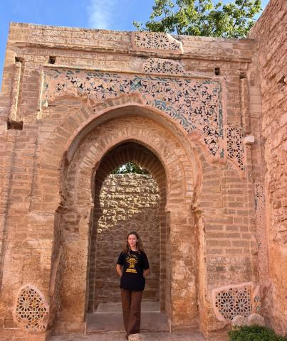 I stand underneath an arch in the Ruins of Chellah. The arch is decorated with alicatado-type blue tiles.