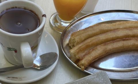 One cup of hot chocolate on the left and three churros on a silver plate on the right. 