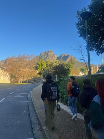 Image of three students walking to school with backpacks on with the iconic devils peak and table mountain in the background. 