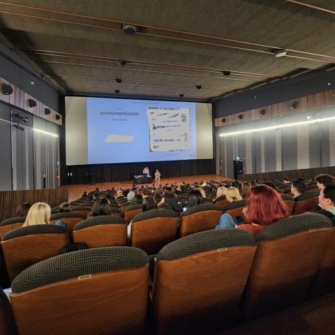 Students seated in a large movie theater listening to an orientation presentation on a screen.