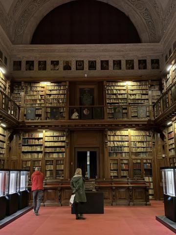 A shot of inside the library at the museum. A red carpet lines the floor and two stories of bookshelves hold hundreds of books.