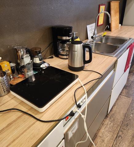 A shared office kitchen with coffee machines, an induction stove, a sink, and kitchen appliances.