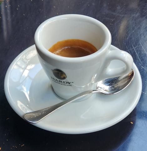 A small cup of Italian espresso served on a white saucer with a spoon at a café table.