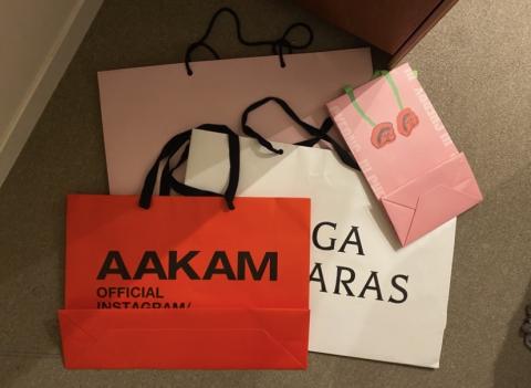 Four shopping bags: two pink, one white, and one red with the text "AAKAM".