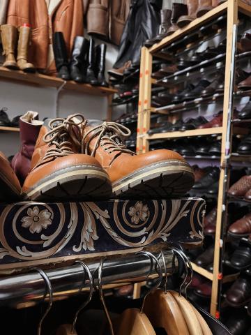 A light brown pair of leather boots sits on a shelf above a wooden clothing rack.