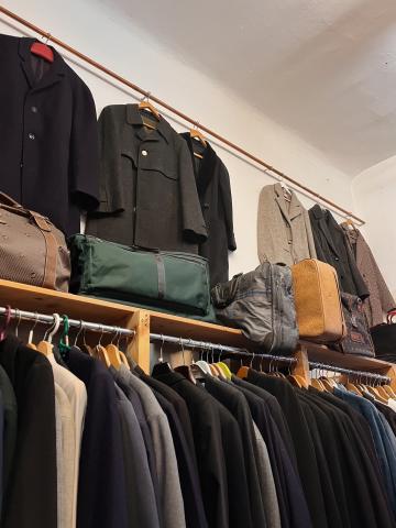 A collection of wool winter coats displayed on a white wall above a wooden clothing rack.