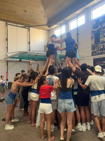 Human pyramid made of large base of students with four students balanced on top of them.