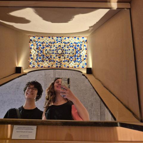 Two students take a mirror selfie with a mocarabe design above them.