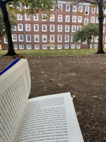 Open book in public garden with brick building and trees in background