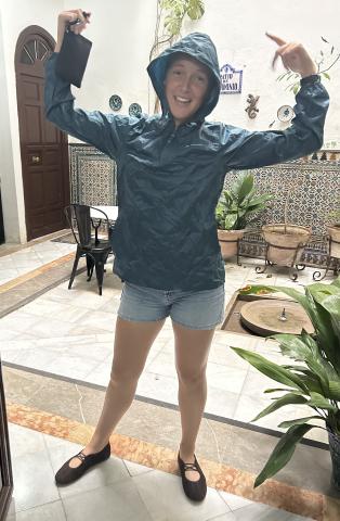 Student wearing brown flats, denim shorts, and a blue pullover rainjacket