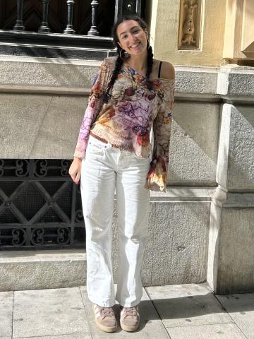 student wearing flowy purple and tan shirt with lots of symbols and colors on it, white jeans with a brown belt, and brown sneakers
