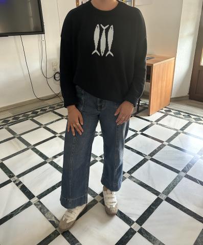 Student wearing white sneakers, jeans, and a navy sweater with fish on it.