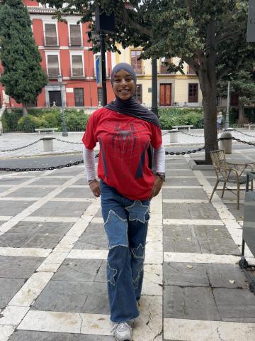 Student waring jeans with stars on them, spiderman tee shirt layered on top of a white shirt, and a dark mauve hijab.