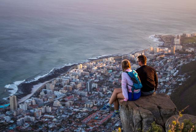 two students sit on the edge of a mountain above Cape Town's city and coast line
